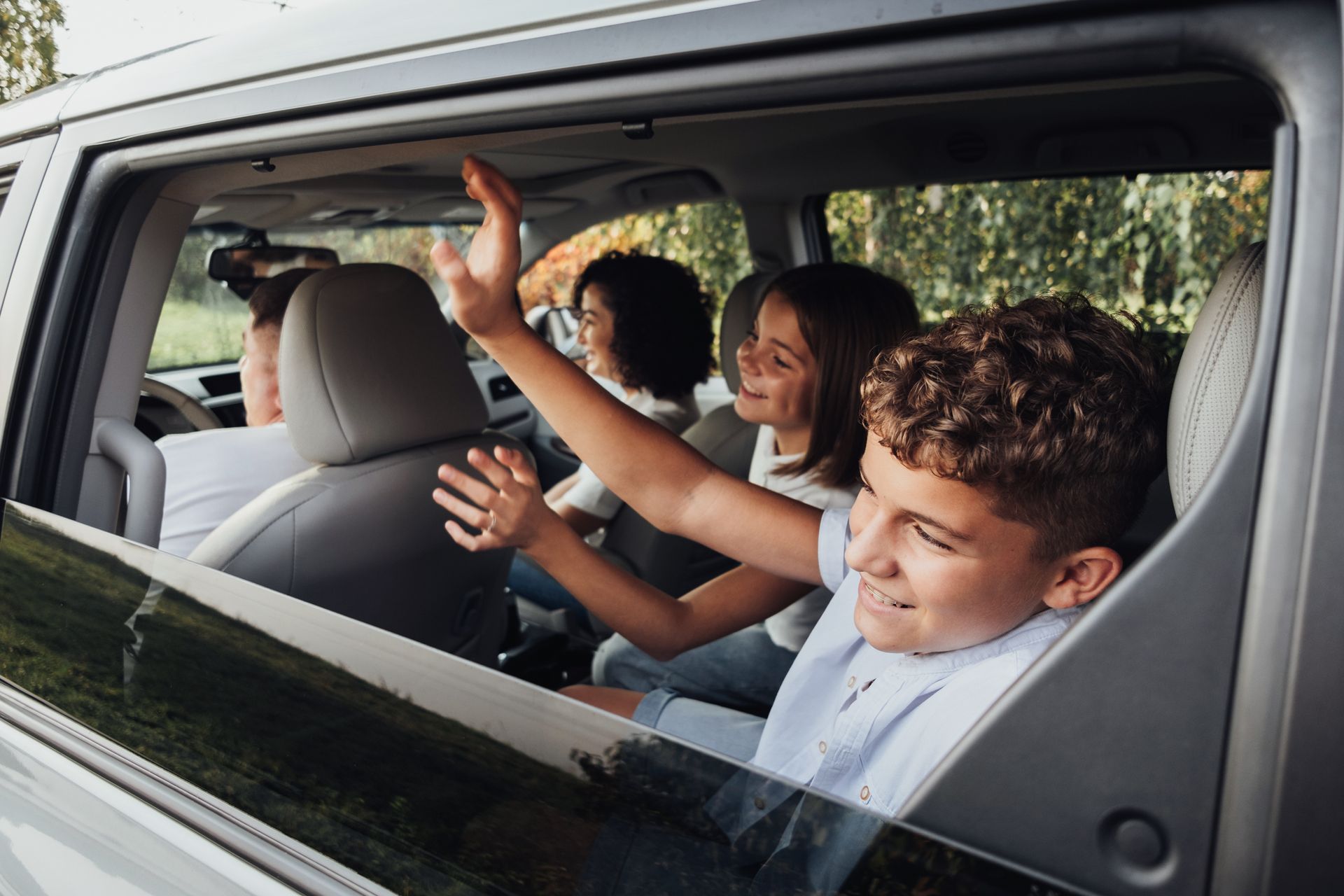 Trois personnes sourient et font signe de la main depuis la banquette arrière d'une voiture.