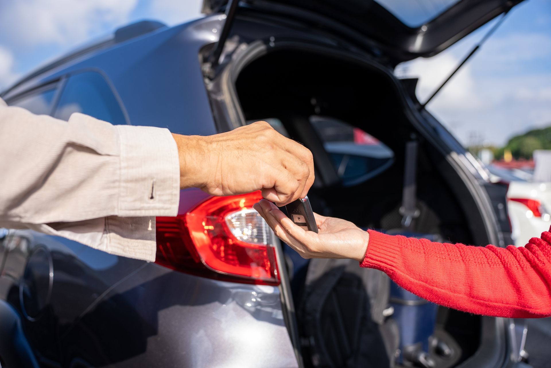 Des mains passent un petit objet dans le coffre ouvert d'une voiture à l'extérieur.