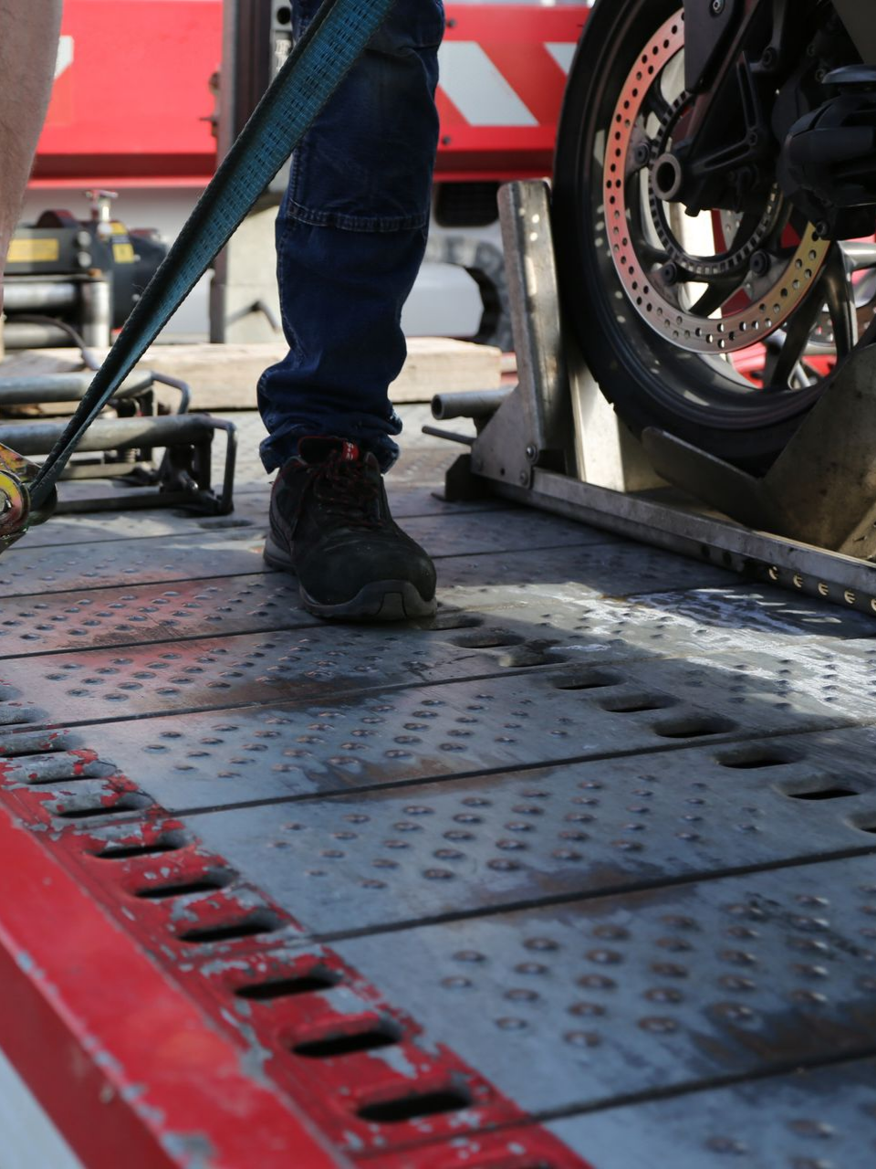 Une personne attache une moto avec une sangle sur le plateau d'une dépanneuse. 