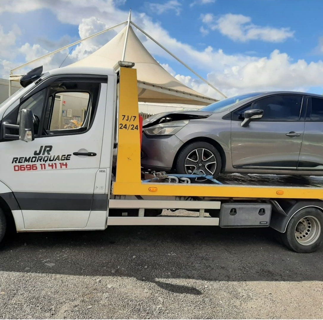 Dépanneuse avec une voiture argentée endommagée sur son plateau.