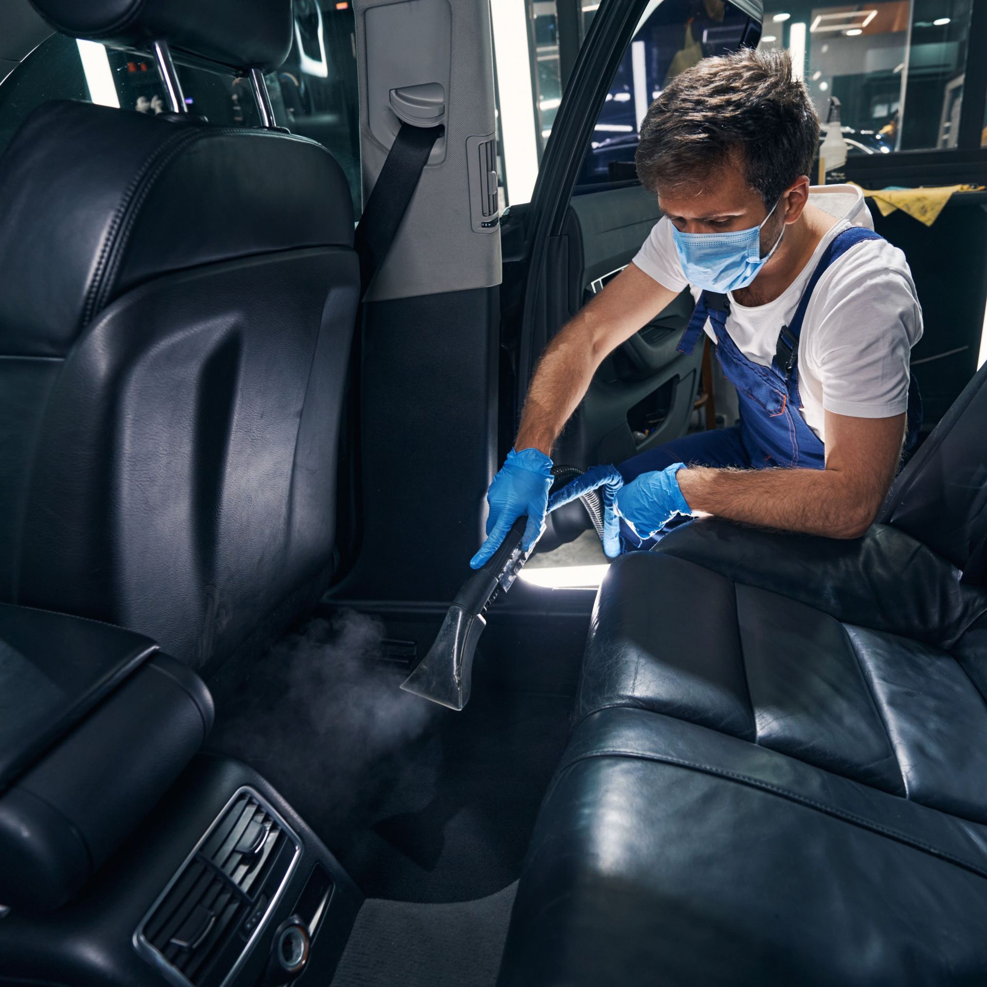 Un hombre que lleva una máscara y guantes está limpiando el asiento trasero de un automóvil.