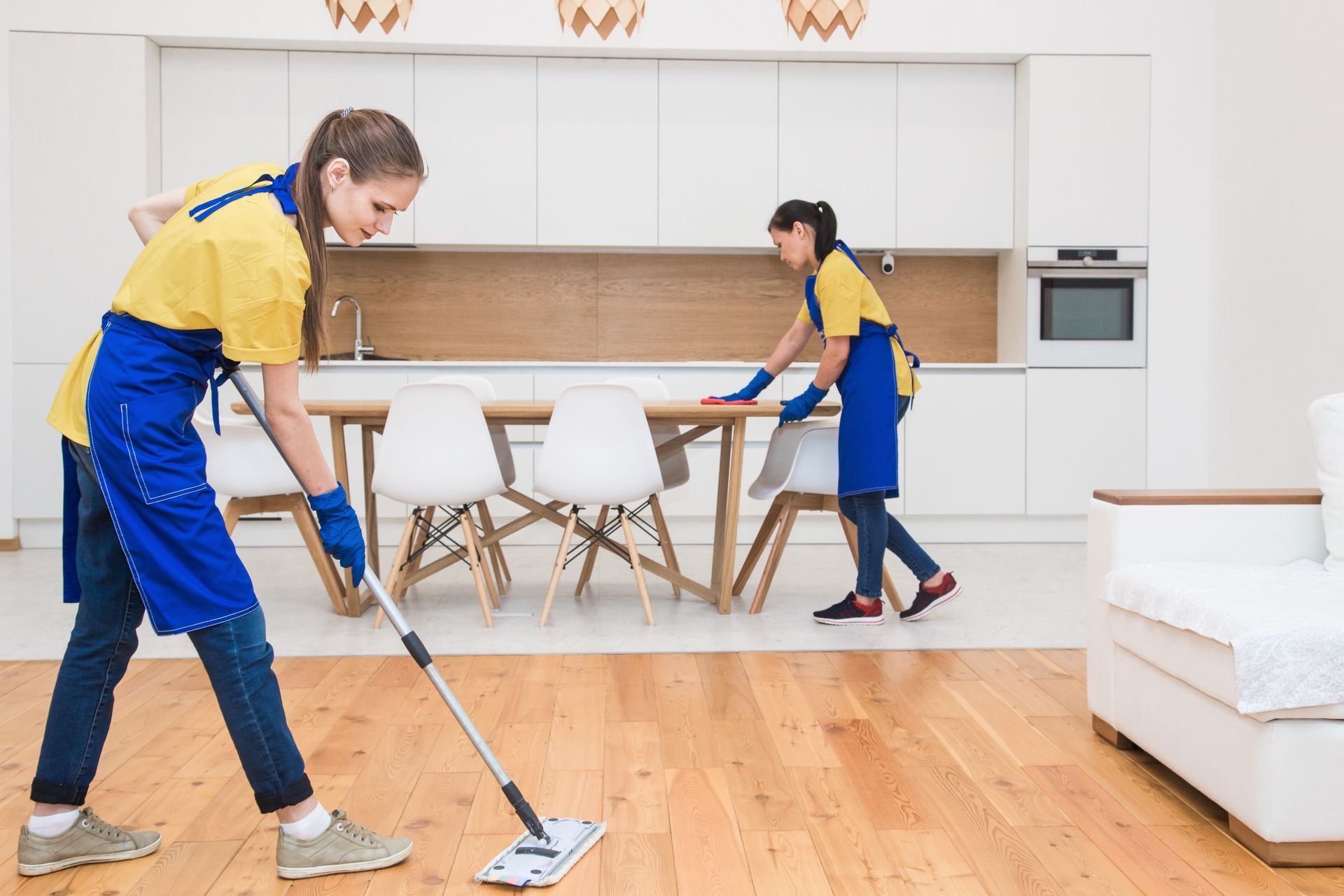 Dos mujeres están limpiando un piso de madera en una sala de estar.