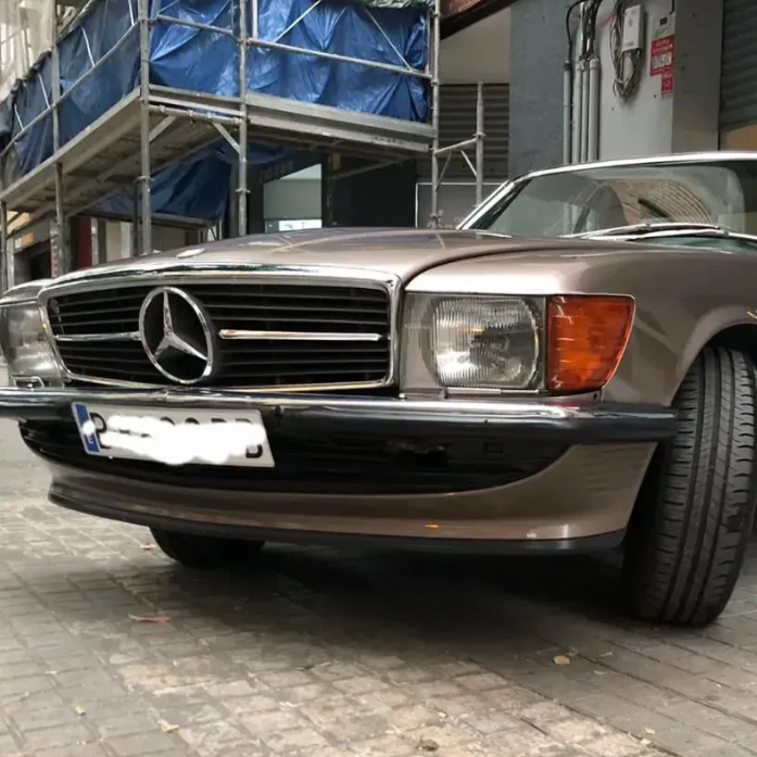 Persona trabajando en el motor de un coche con una llave inglesa. Al aire libre, en un entorno soleado.
