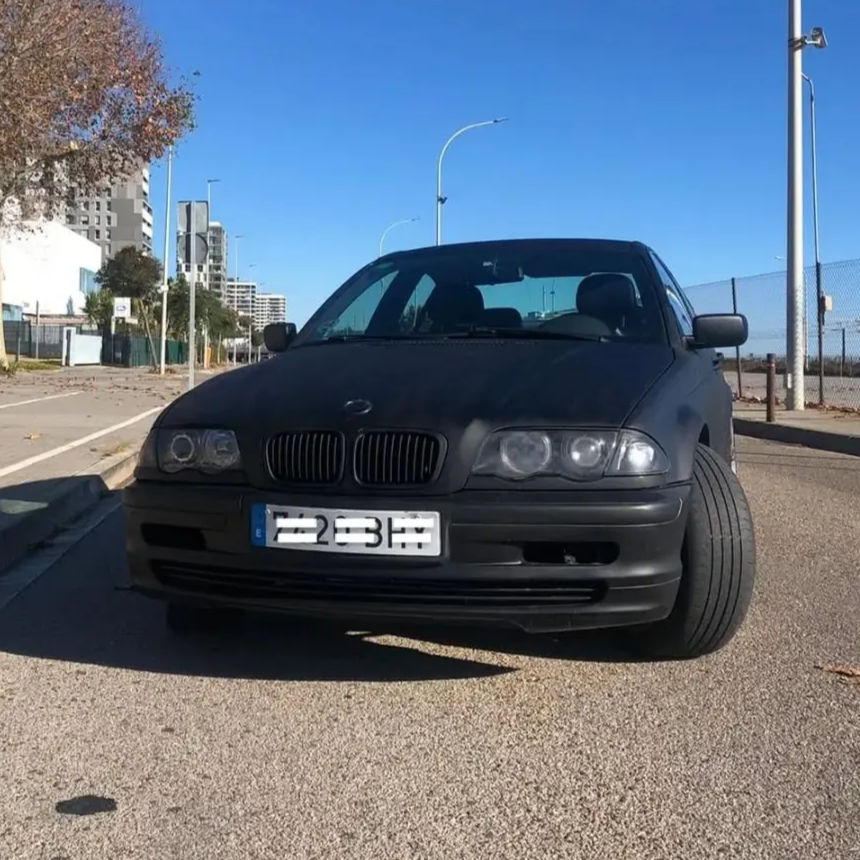 Un sedán BMW negro estacionado en una calle de la ciudad en un día soleado.