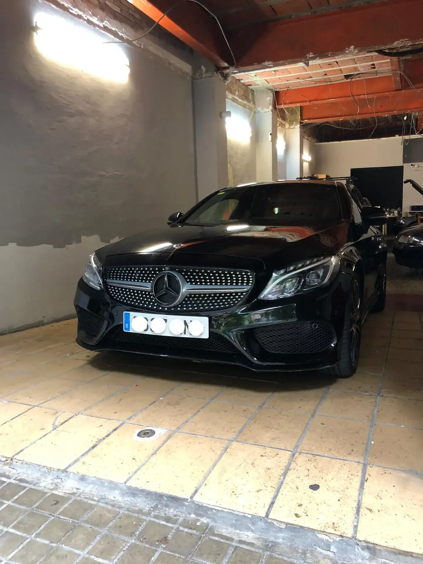 Sedán Mercedes-Benz negro estacionado en el interior sobre piso de baldosas con la puerta del garaje abierta.