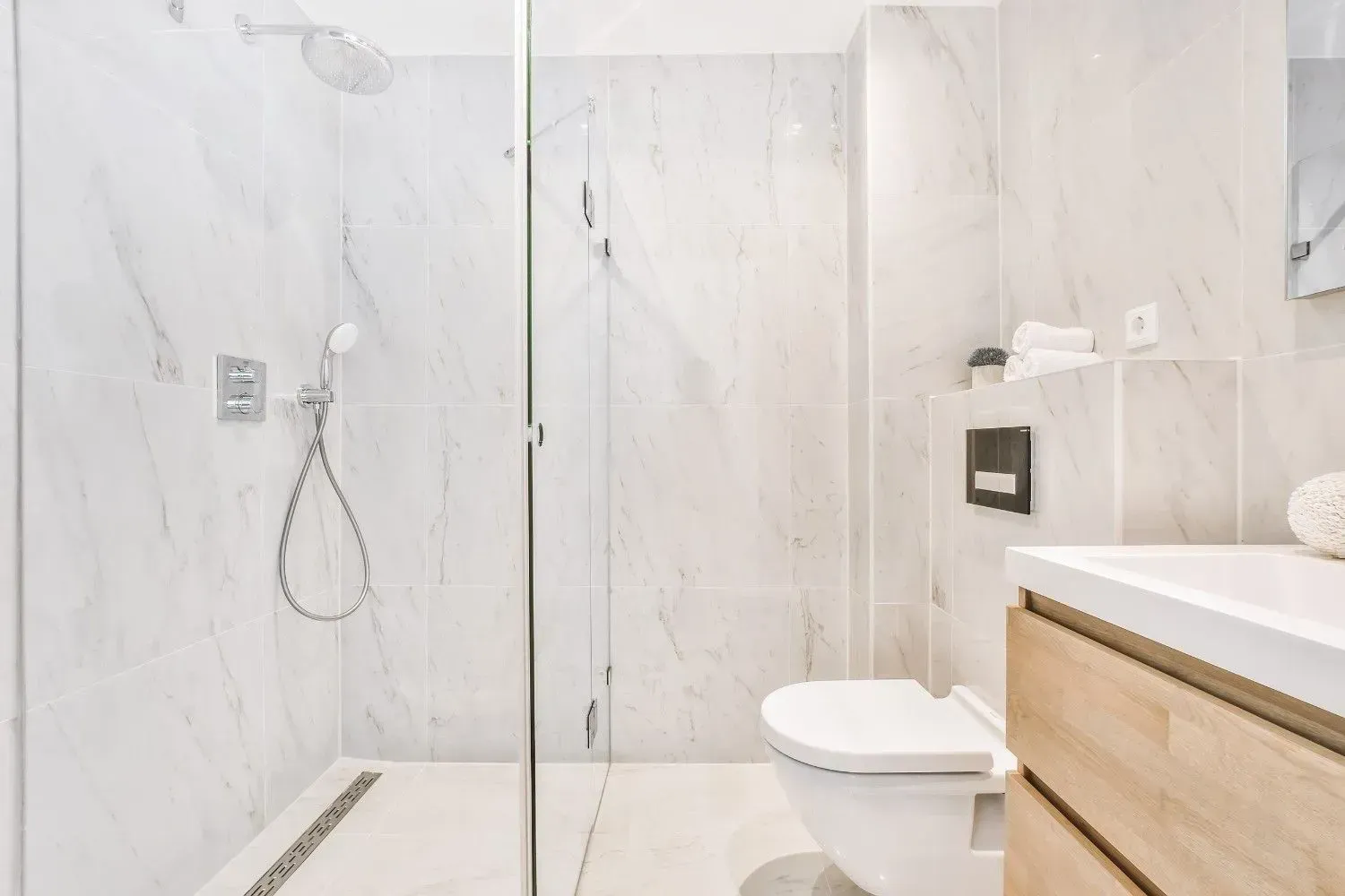 Baño moderno blanco con ducha de cristal, inodoro y encimera de madera.