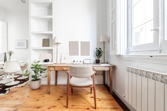Despacho minimalista en color blanco con escritorio de madera, silla, plantas y luz natural proveniente de la ventana.