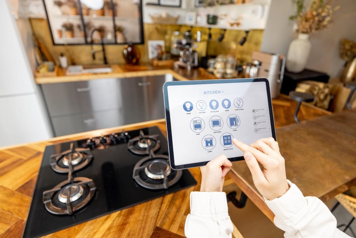 Persona utilizando una tableta para controlar una placa de gas negra en una cocina moderna.
