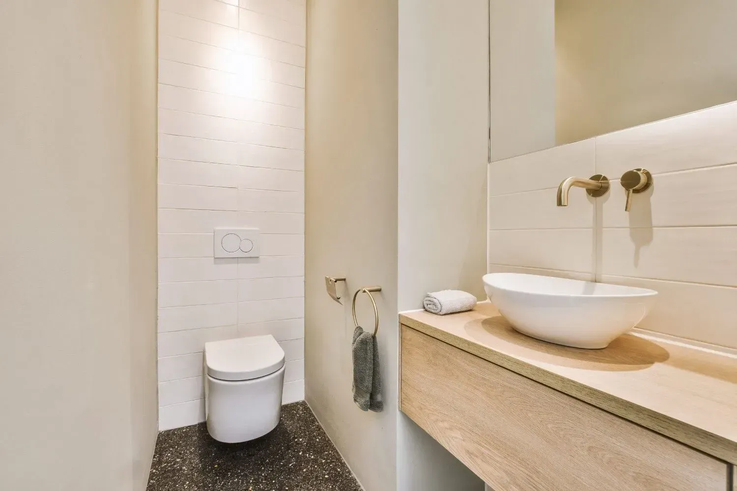Baño minimalista con inodoro suspendido y lavabo con grifería de latón.