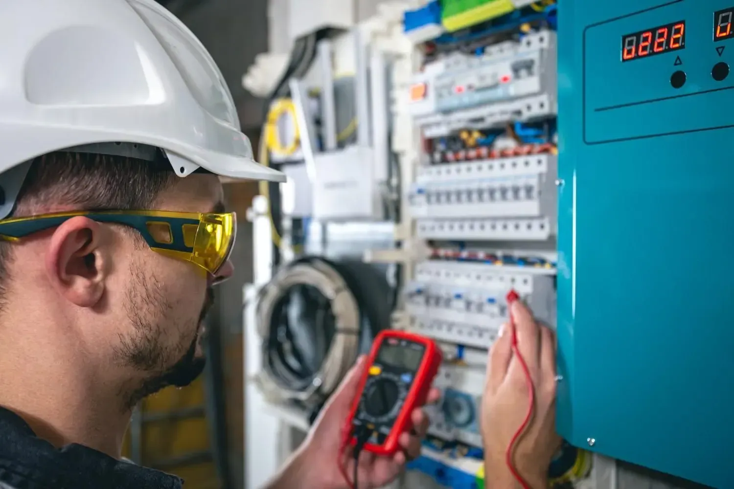 Técnico con casco revisando un panel eléctrico con un multímetro en un cuarto de servicio.