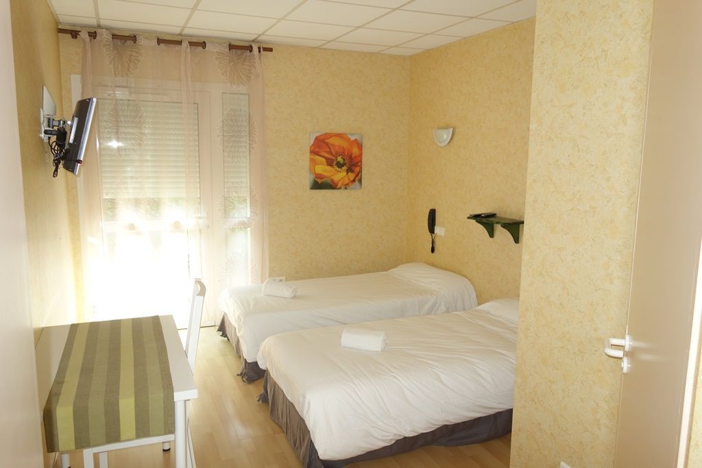 Petite chambre d’hôtel avec deux lits jumeaux, des rideaux aux fenêtres et une peinture murale.