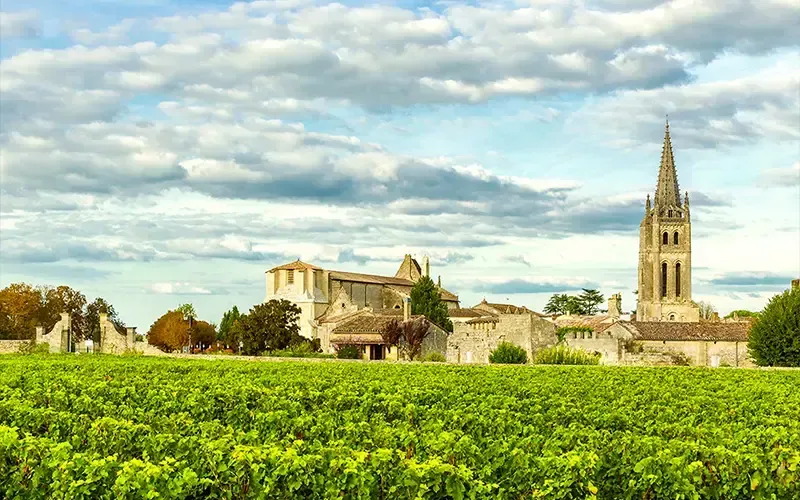 Le clocher d’une église de village se dresse au-dessus de champs verdoyants sous un ciel partiellement nuageux