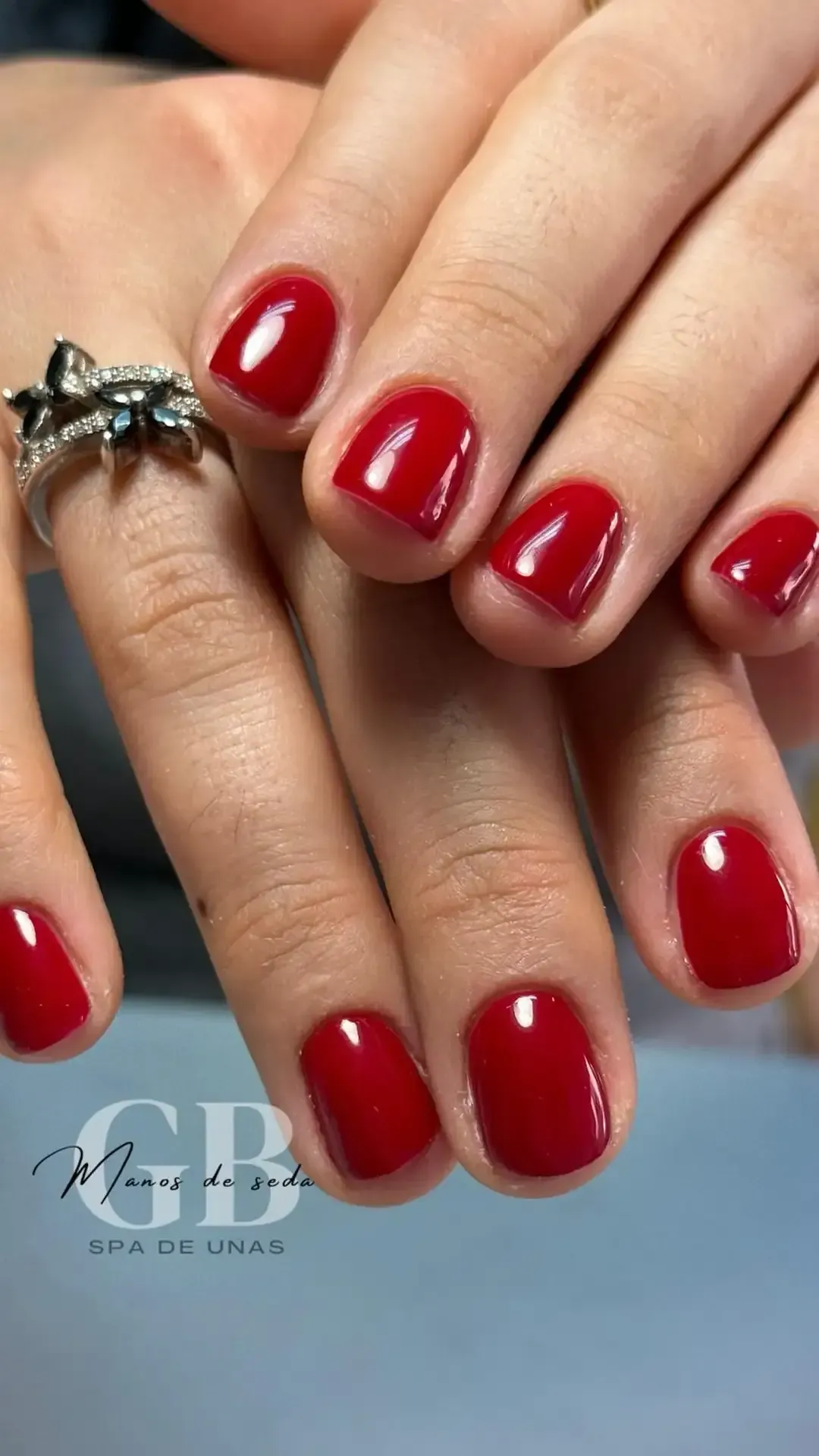 Uñas cortas y cuadradas con esmalte rojo; un anillo de plata en un dedo.