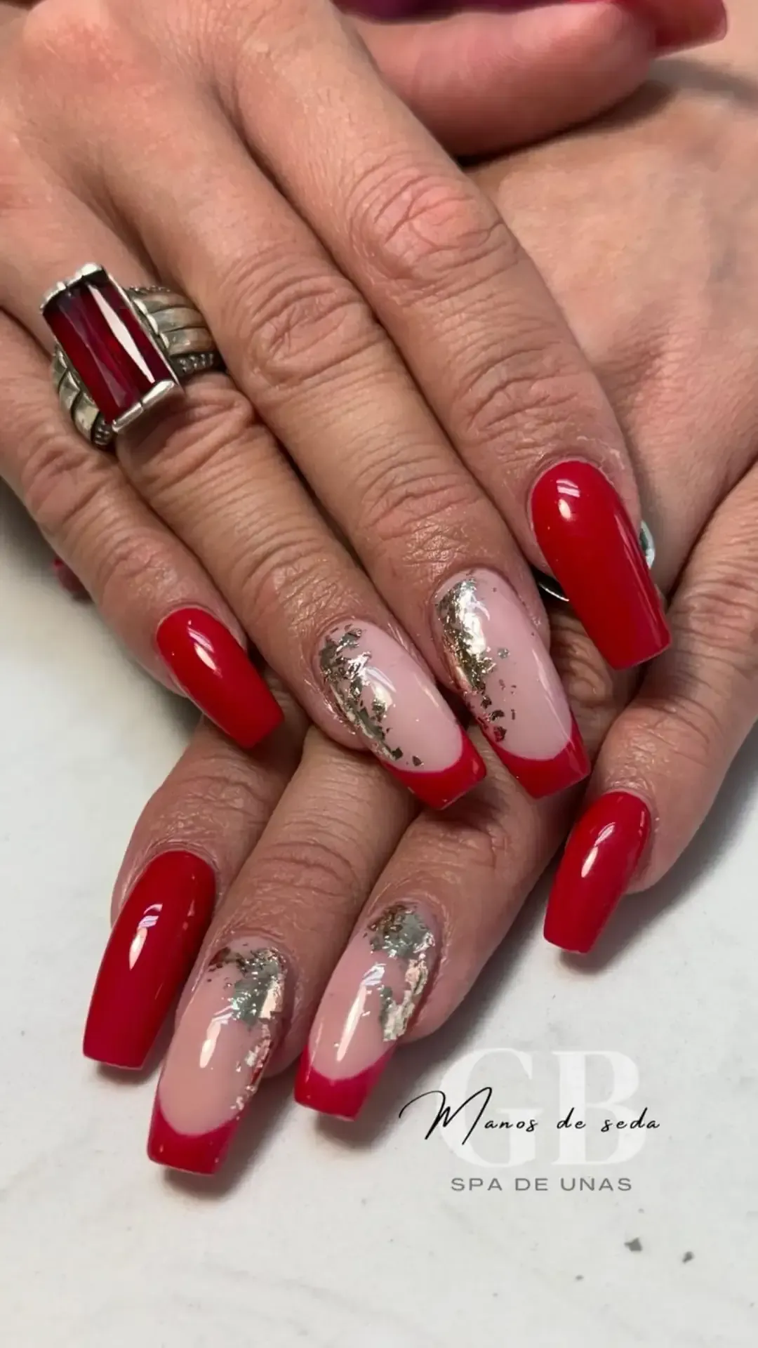 Primer plano de unas manos con uñas decoradas en rojo y con purpurina. Una uña lleva manicura francesa.