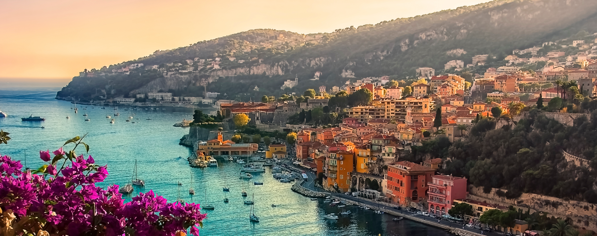 Colorful coastal town on a hillside beside a turquoise bay at sunset.