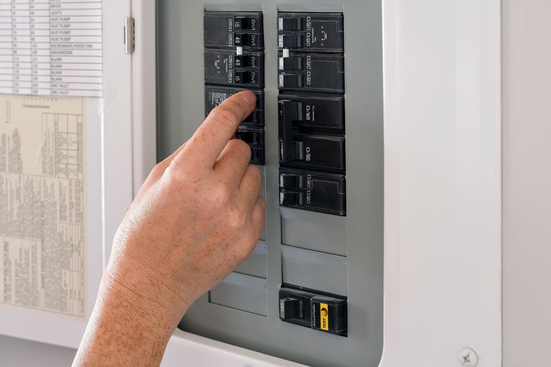Une main actionne un interrupteur dans un tableau électrique gris.