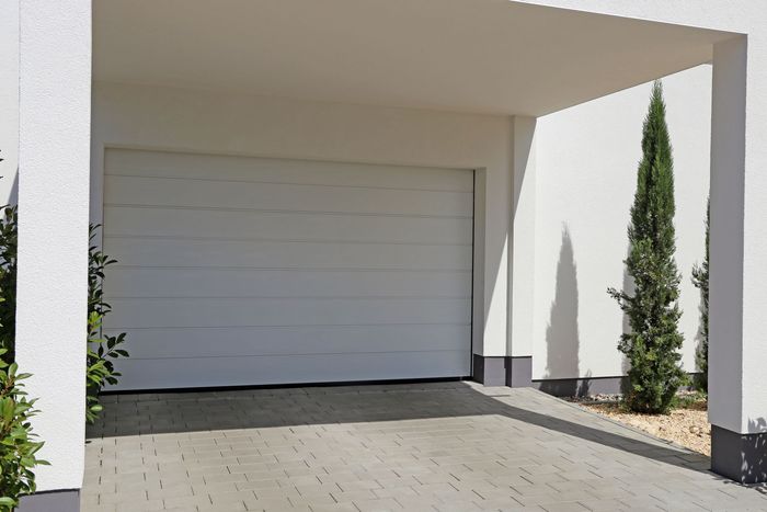 Garage moderne blanc avec porte fermée et un petit arbre près de l'entrée