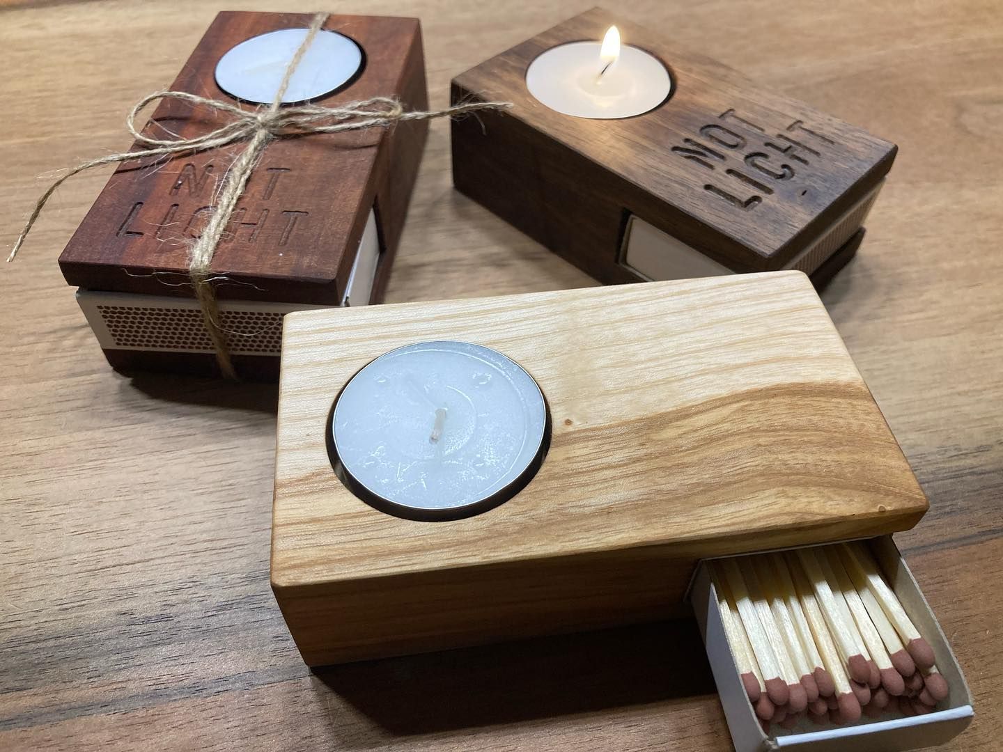 Drei hölzerne Kerzenständer mit Streichhölzern darin auf einem Holztisch.