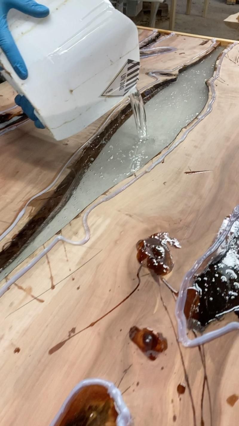 Eine Person gießt flüssiges Giessharz auf einen Holztisch.