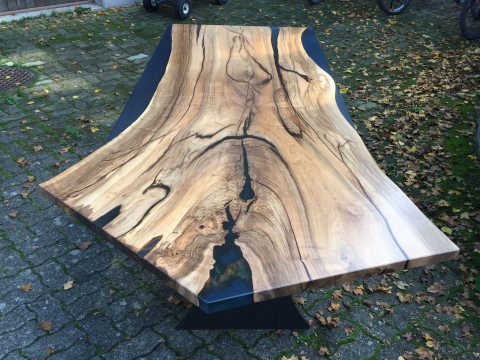 Ein Holztisch mit schwarzem Untergestell steht auf einem gepflasterten Gehweg.