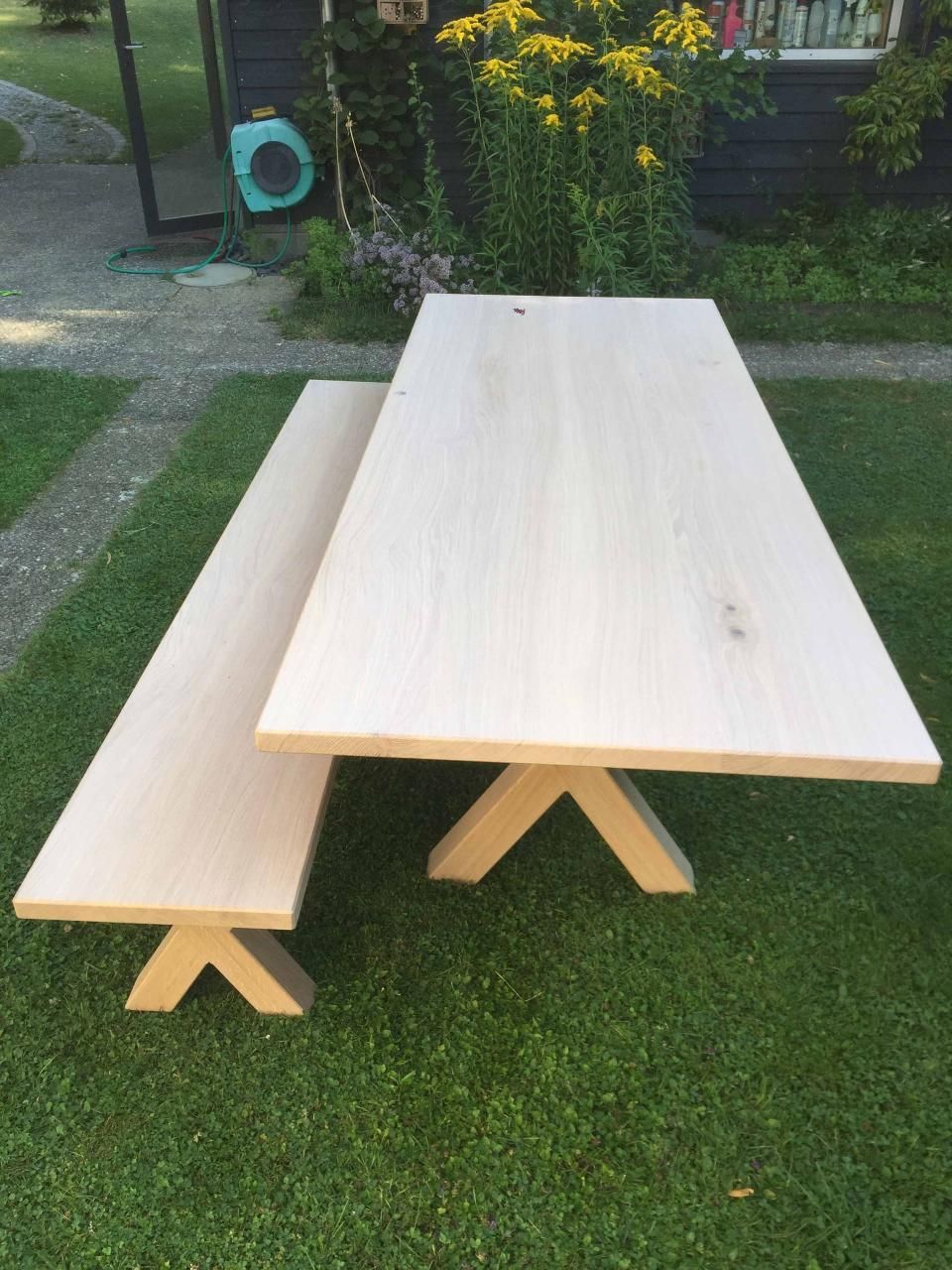 Ein hölzerner Picknicktisch und eine Bank stehen auf einem üppigen grünen Rasen.