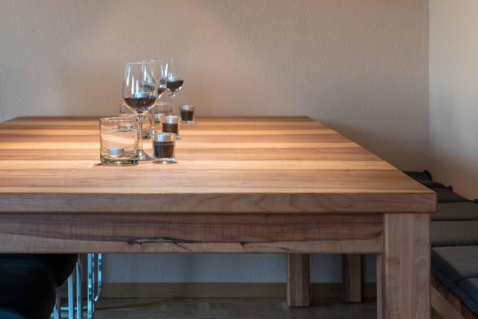 Ein Holztisch mit Weingläsern und Kerzen darauf.