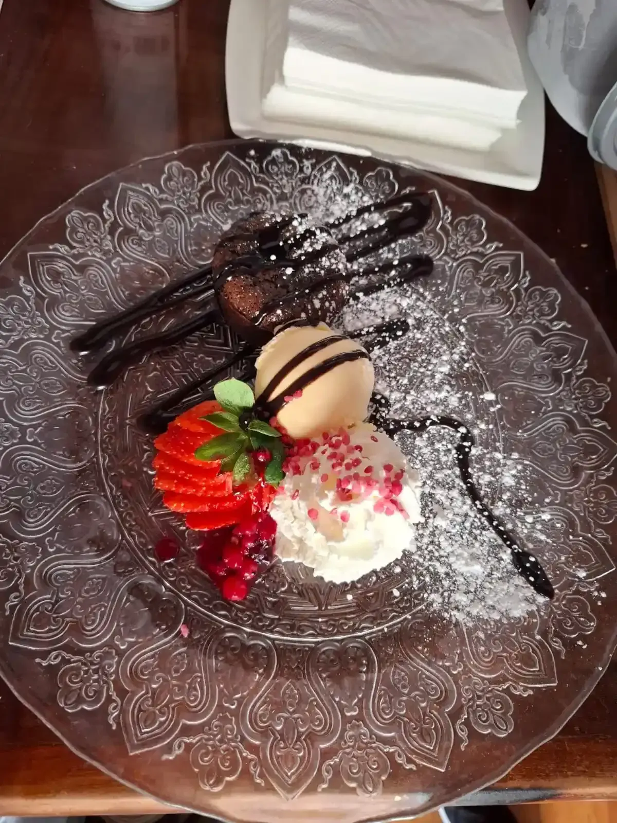 Postre de chocolate con fresas, crema batida y sirope en un plato de cristal.