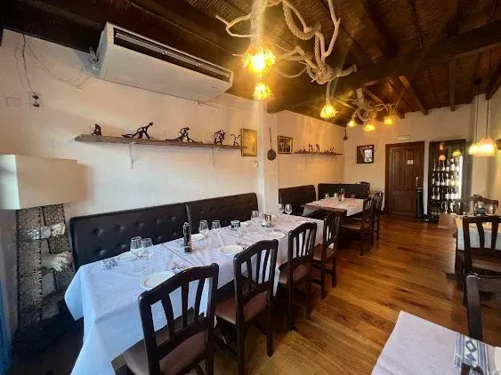 Elegante comedor de restaurante con manteles blancos, sillas oscuras, suelos de madera e iluminación cálida.