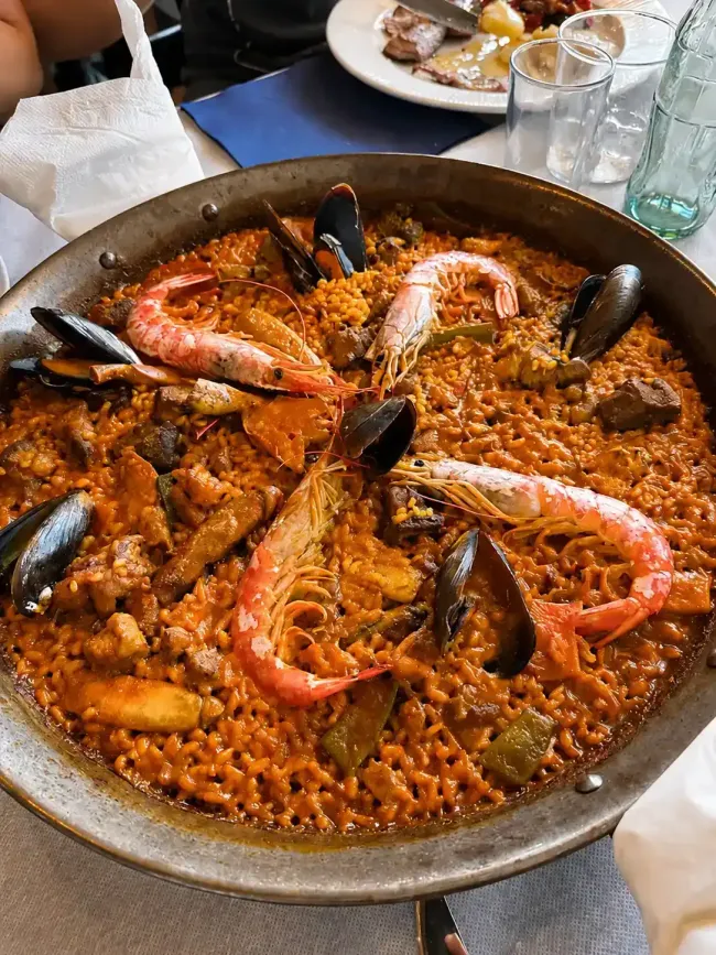 Paella de marisco en una sartén, cubierta con gambas y mejillones, sobre una mesa de comedor.