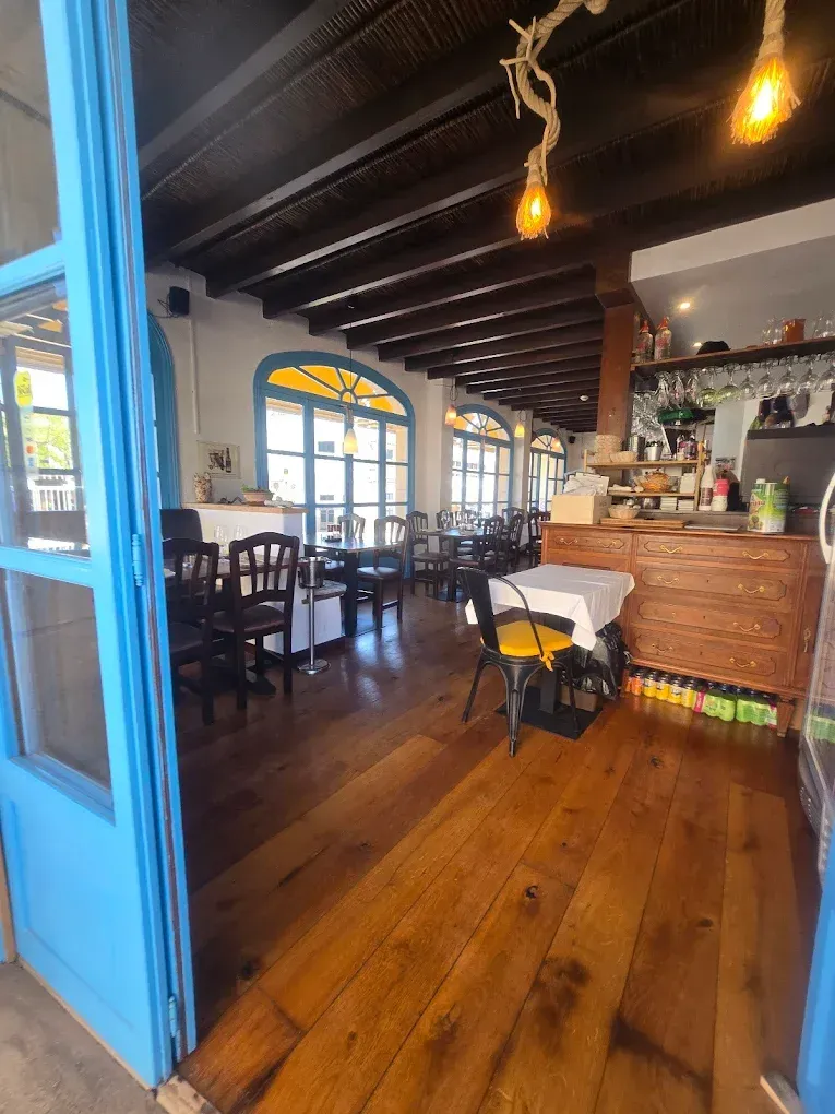 Interior vacío de una cafetería con suelos de madera, lámparas colgantes y una puerta azul.