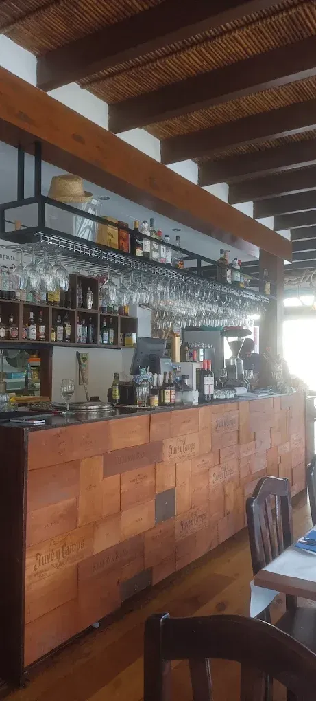 Interior de bar de madera con cristalería colgante, botellas y taburetes altos bajo vigas a la vista.
