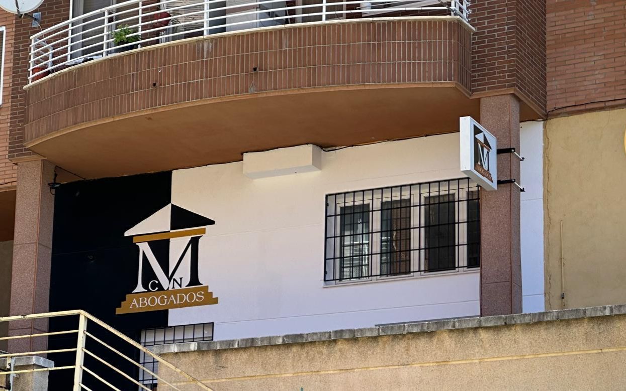 Fachada de un edificio, mitad negra y mitad blanca, con el logotipo de una inmobiliaria. Debajo, un balcón con ventanas y rejas.