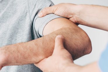 Physiotherapeut behandelt Oberarm eines Patienten