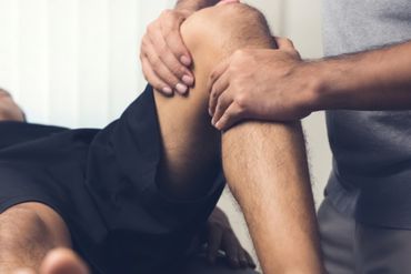 Physiotherapeut behandelt Knie eines Patienten