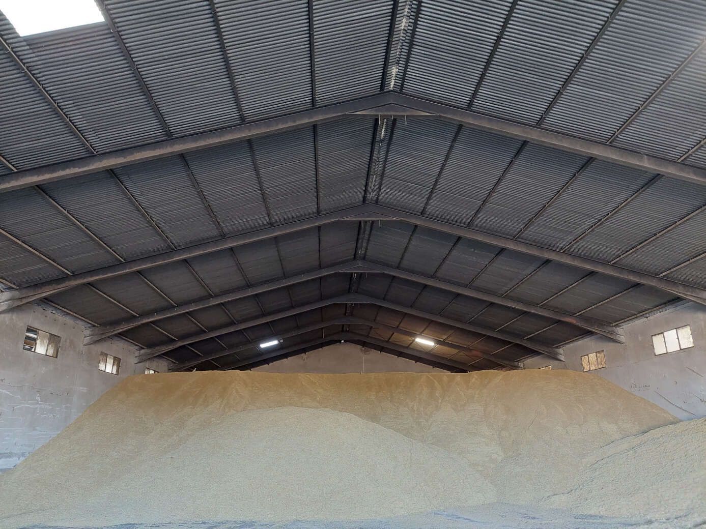 Gran cobertizo de almacenamiento cubierto con un alto techo metálico arqueado sobre pilas de material.