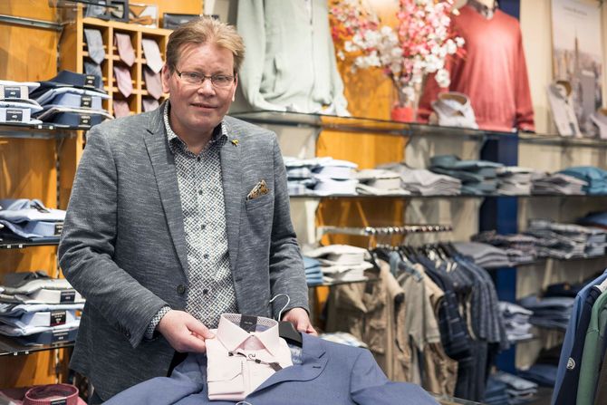 Ein Mann im Anzug steht in einem Bekleidungsgeschäft und hält ein Hemd in der Hand.