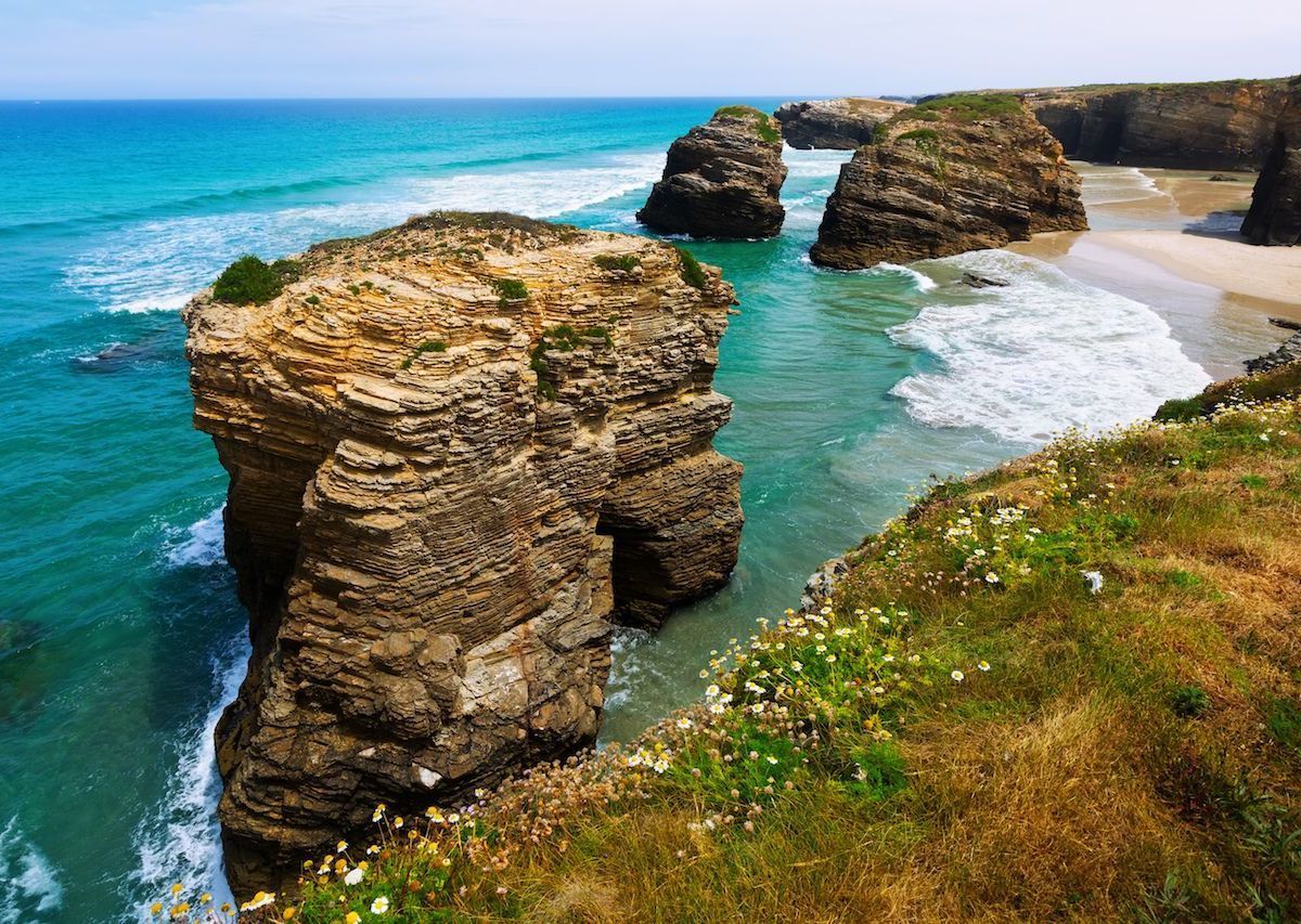 Acantilados rocosos y playa de arena con agua turquesa bajo un cielo despejado.