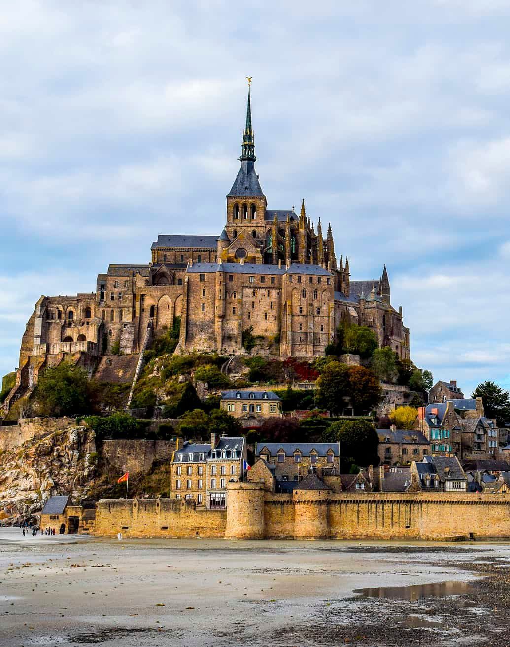 Mont Saint-Michel, Francia: Monasterio  medieval en lo alto de una isla rocosa, bajo un cielo nublado.