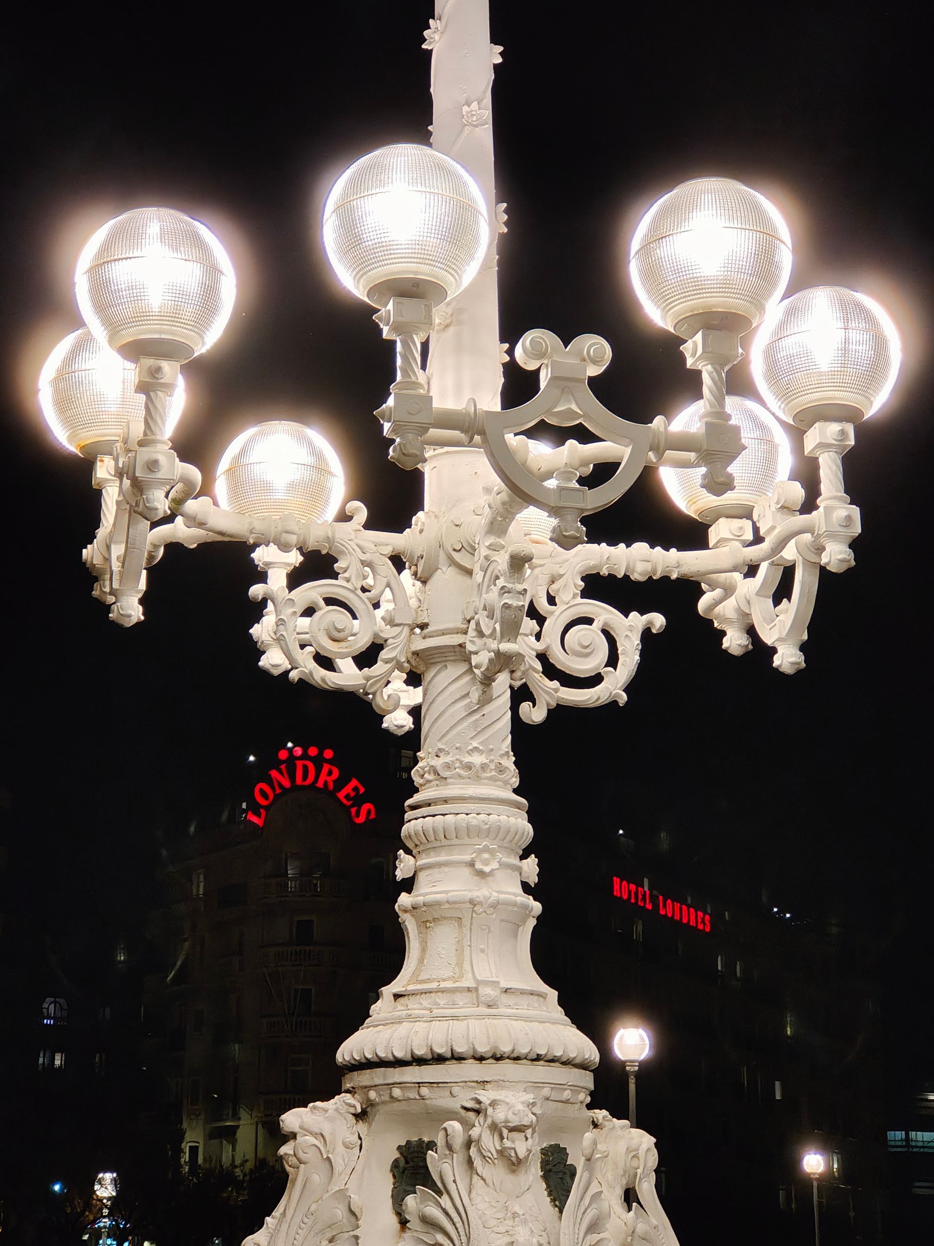 Farola blanca adornada con múltiples bombillas brillantes contra un cielo nocturno oscuro.