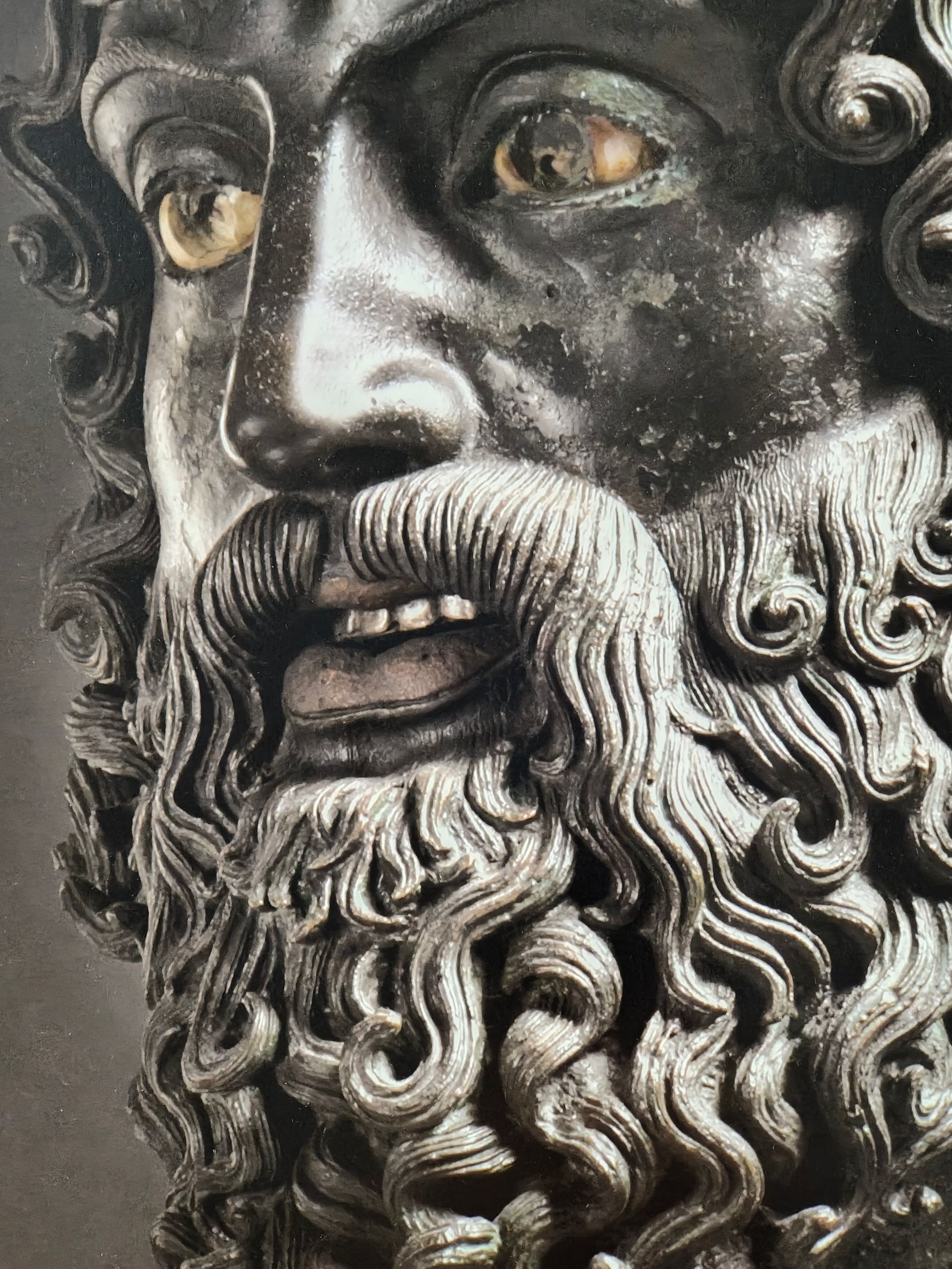 Primer plano de una estatua de bronce de un hombre barbudo con cabello rizado y ojos intensos.