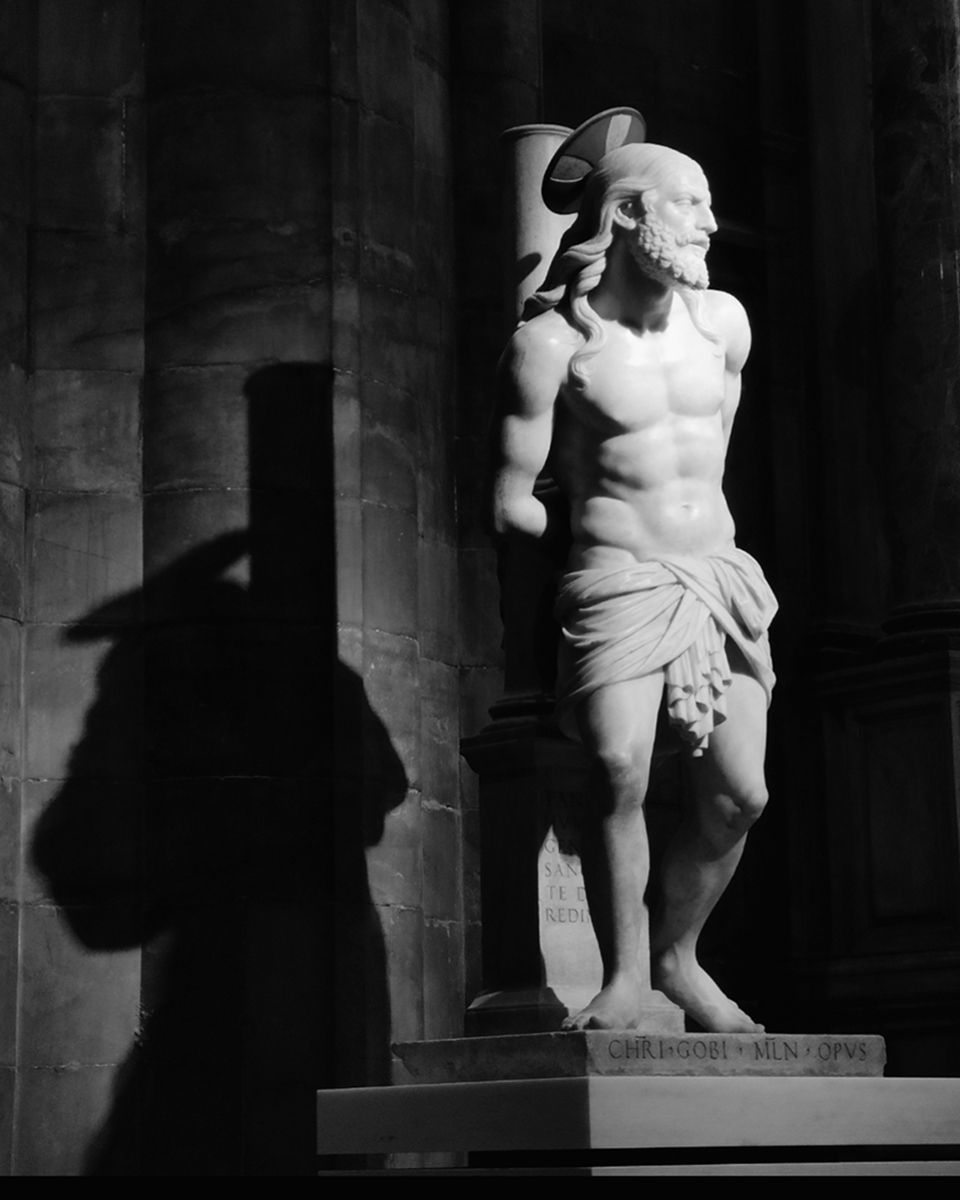 Estatua de un hombre musculoso atado a un pilar, probablemente Jesús. Sombra de la estatua a la izquierda.