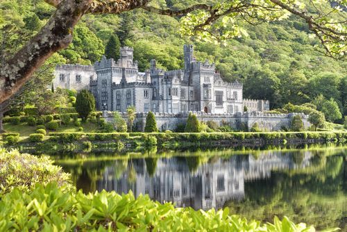 La Abadía de Kylemore reflejada en el lago, rodeada de árboles verdes y follaje.