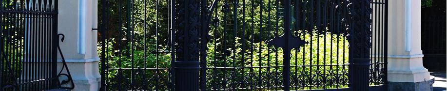 Puerta de hierro negro con columnas y vegetación detrás, en la entrada de un edificio
