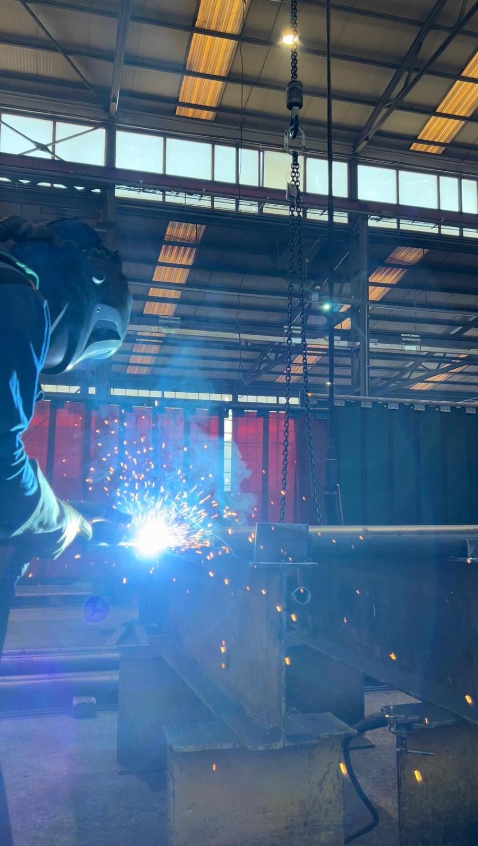 Un homme soude un morceau de métal dans une usine.