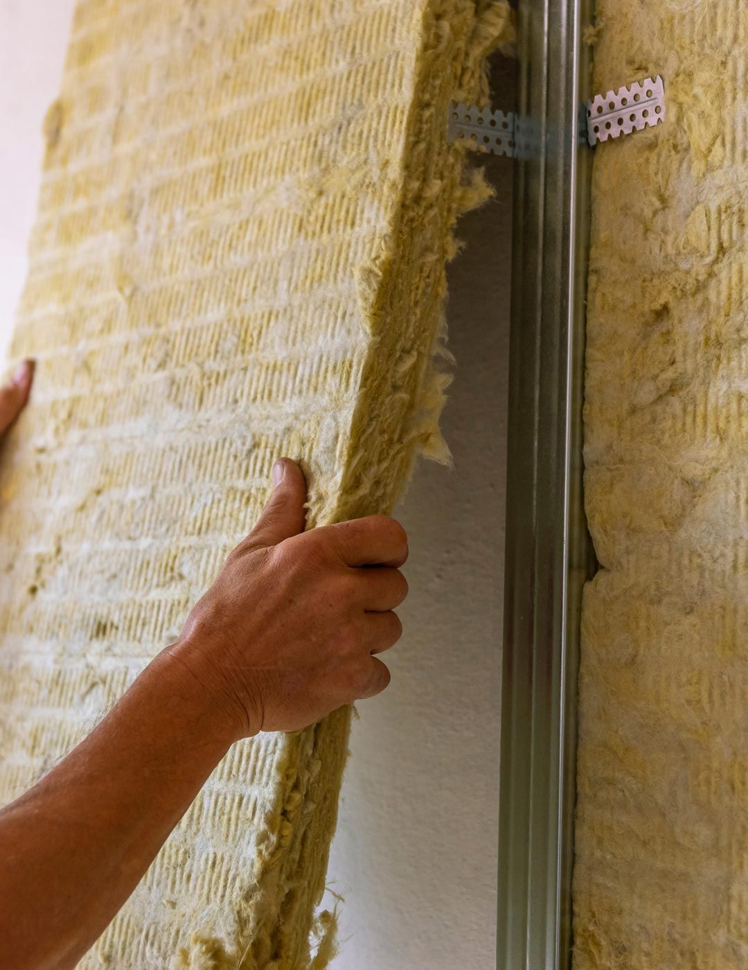 Manos instalando paneles aislantes amarillos en la cavidad de una pared.