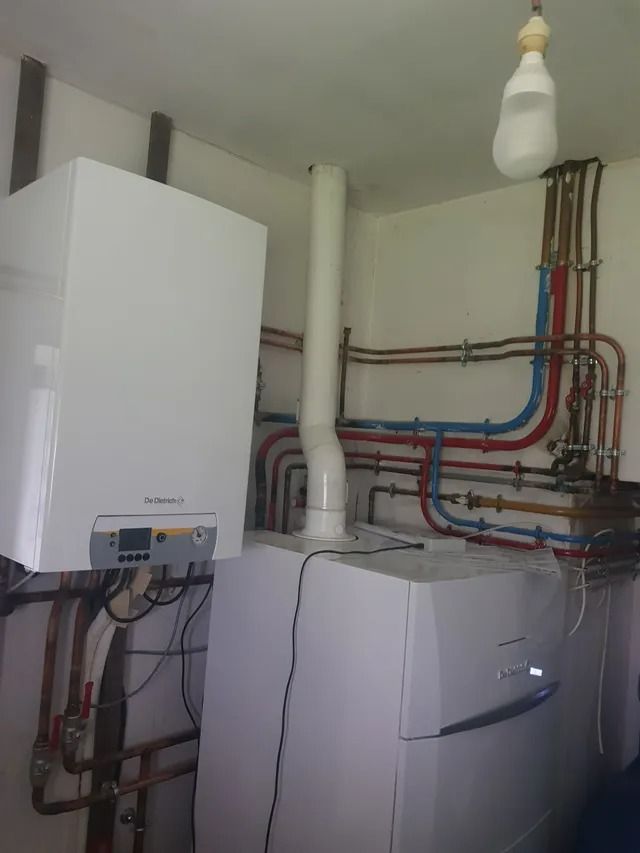 Chaufferie murale avec tuyaux rouges et bleus apparents, armoires blanches et ampoule suspendue