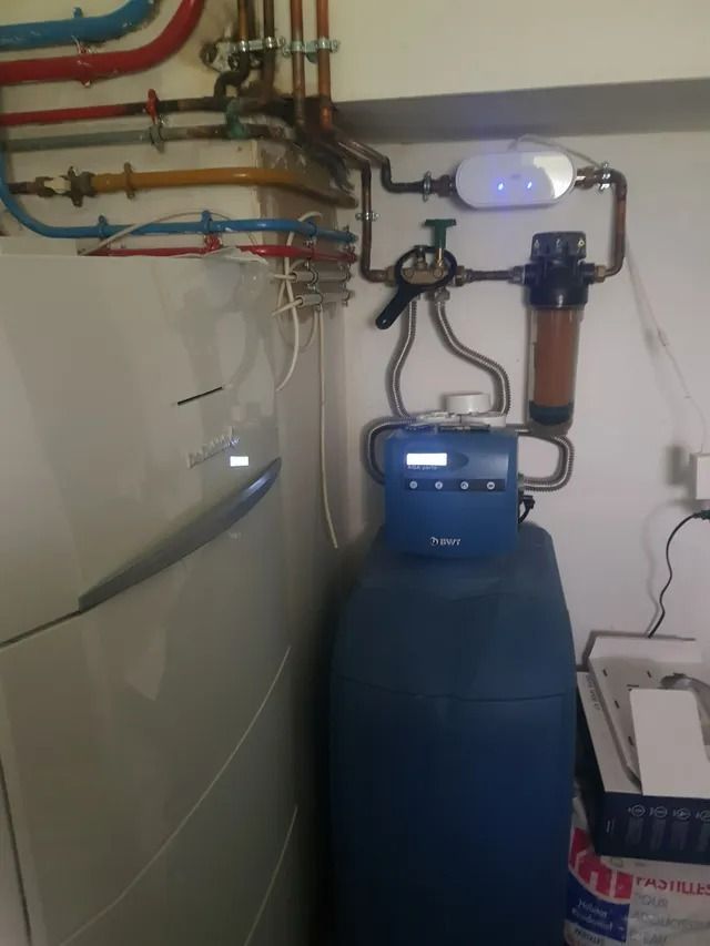 Système de filtration d'eau avec réservoir bleu, tuyaux, manomètres et plomberie murale dans une buanderie