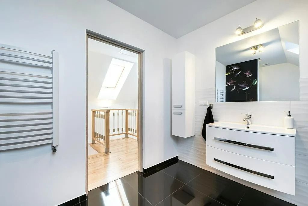 Salle de bains moderne blanche avec meuble-lavabo, miroir, porte-serviettes et porte donnant sur un balcon ensoleillé