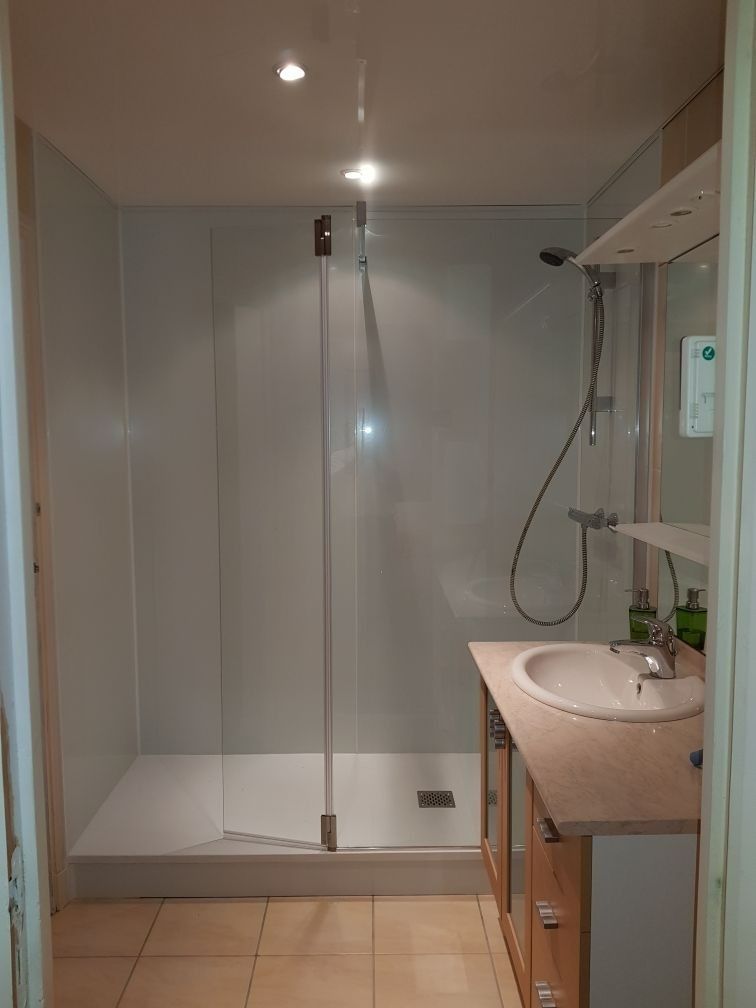 Salle de bains moderne avec douche à l'italienne, porte en verre, meuble vasque et pommeau de douche mural.