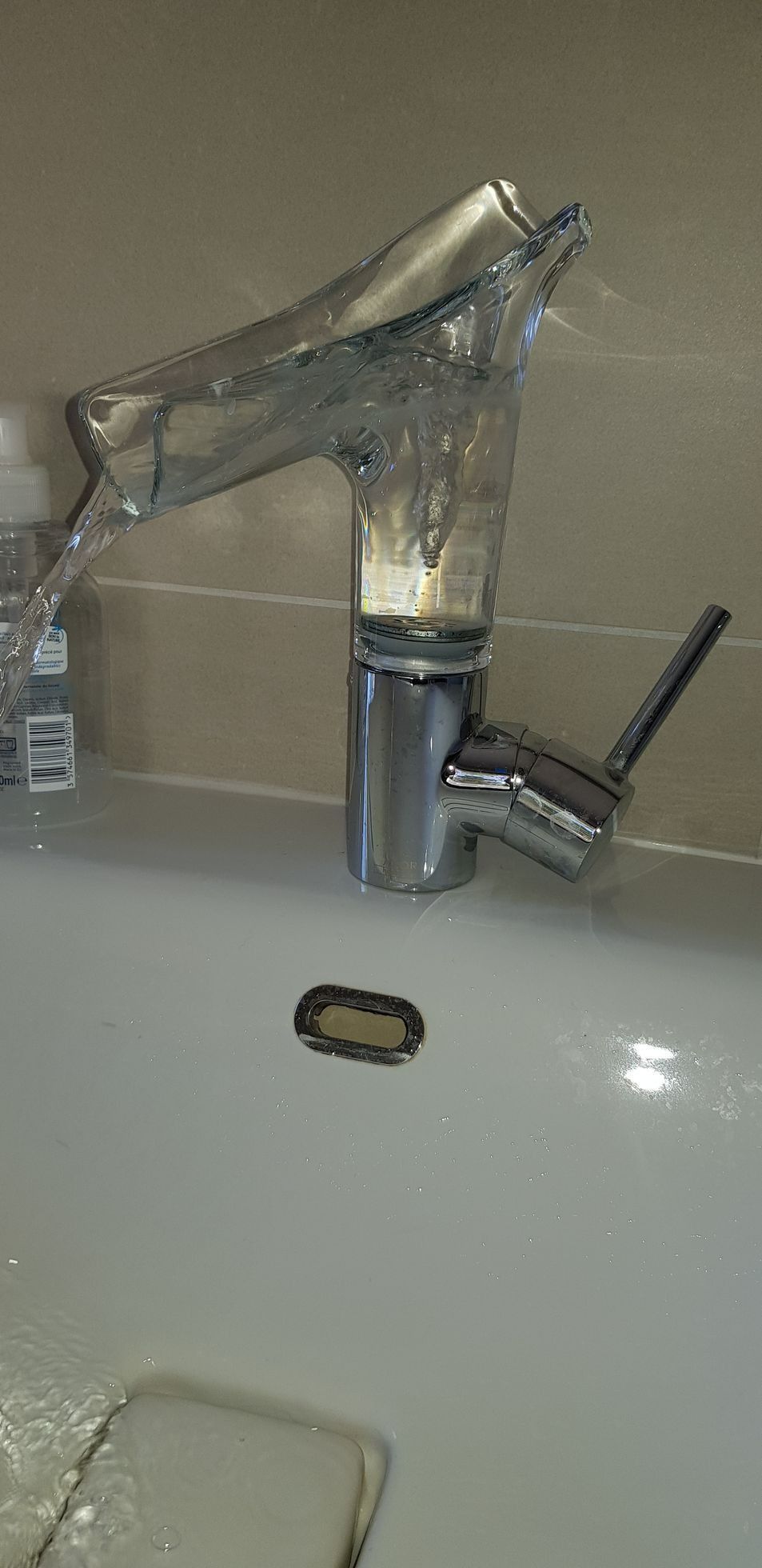 Robinet de salle de bain chromé moderne sur un lavabo blanc, avec un petit porte-savon à proximité.